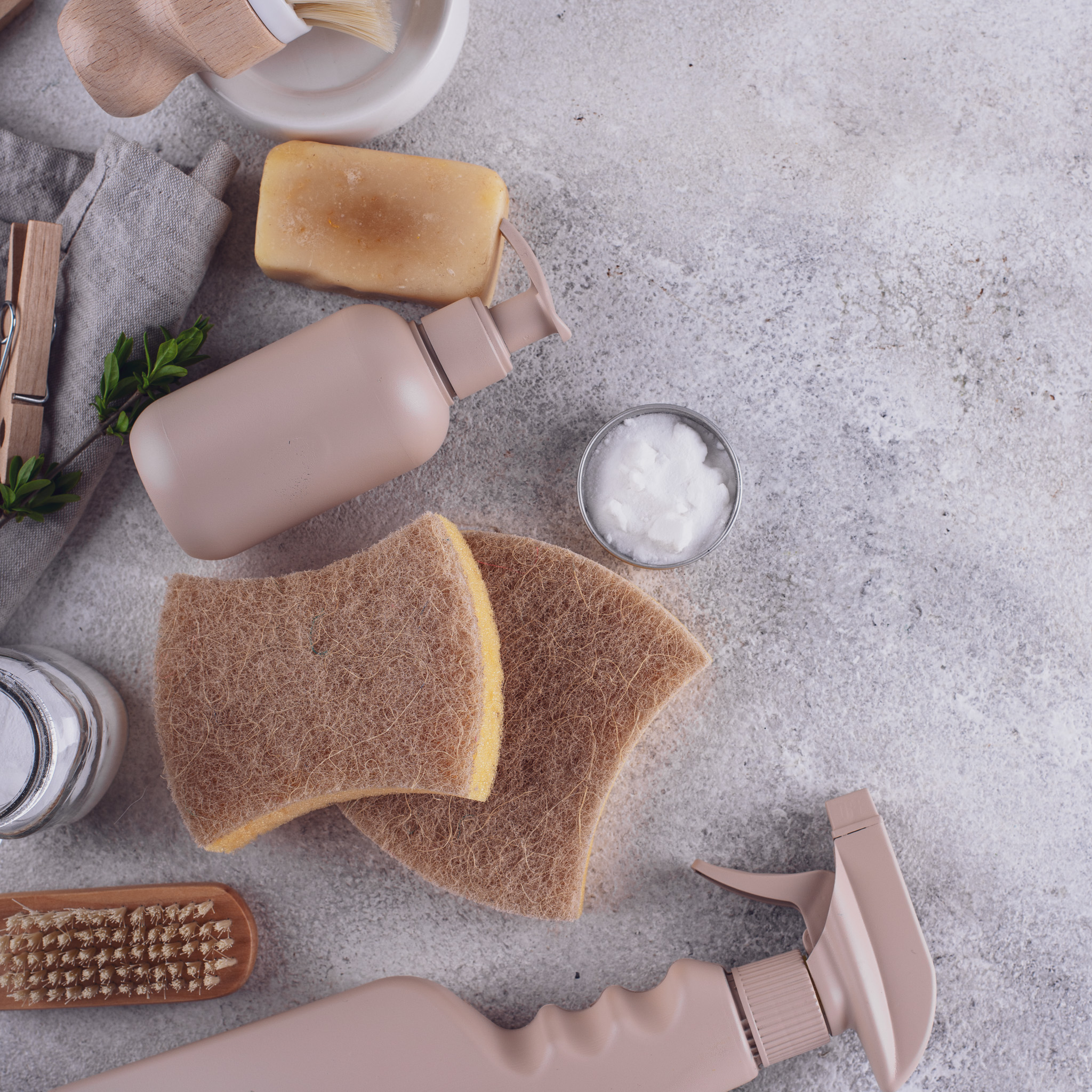 Assortiment d'articles de nettoyage écoresponsables incluant des éponges, du savon, une bouteille rechargeable, une brosse en bois sur un fond de surface texturée. Assortiment d'articles de nettoyage écoresponsables incluant des éponges, du savon, une bouteille rechargeable, une brosse en bois sur un fond de surface texturée.